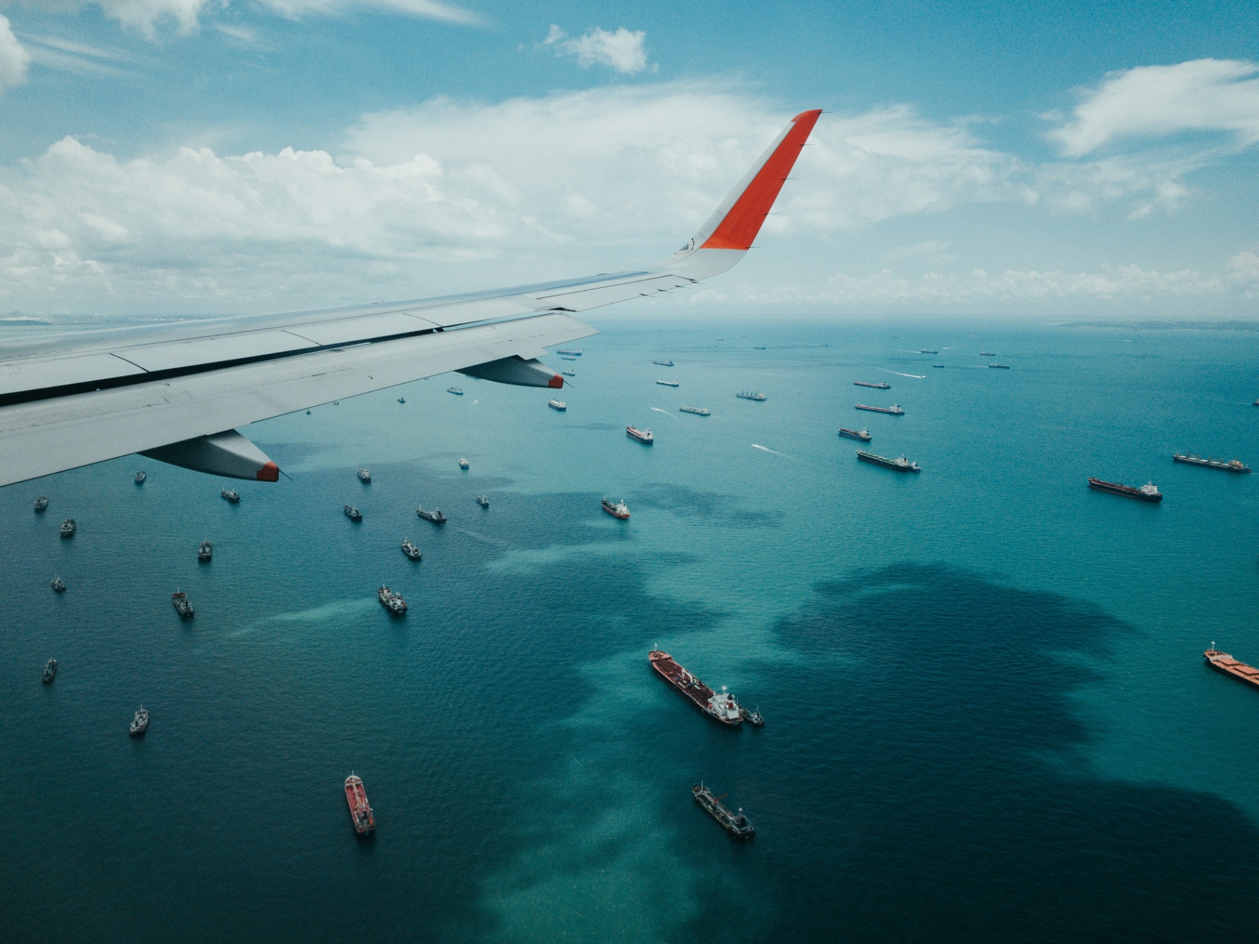 Aerial view of an airplane wing over water with many ships
